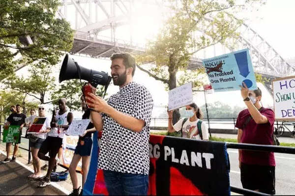 Zohran Mamdani at a rally, wearing a layered smart casual outfit.